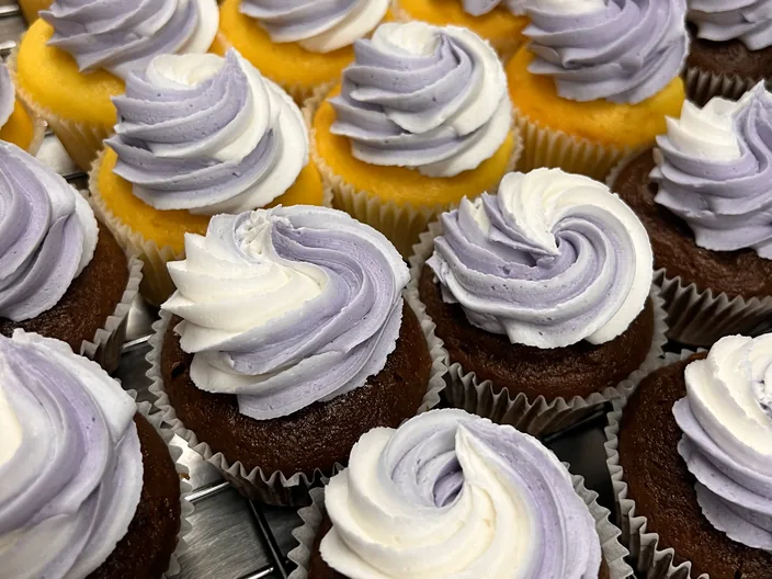 A tray of cupcakes with white and lilac swirled icing.