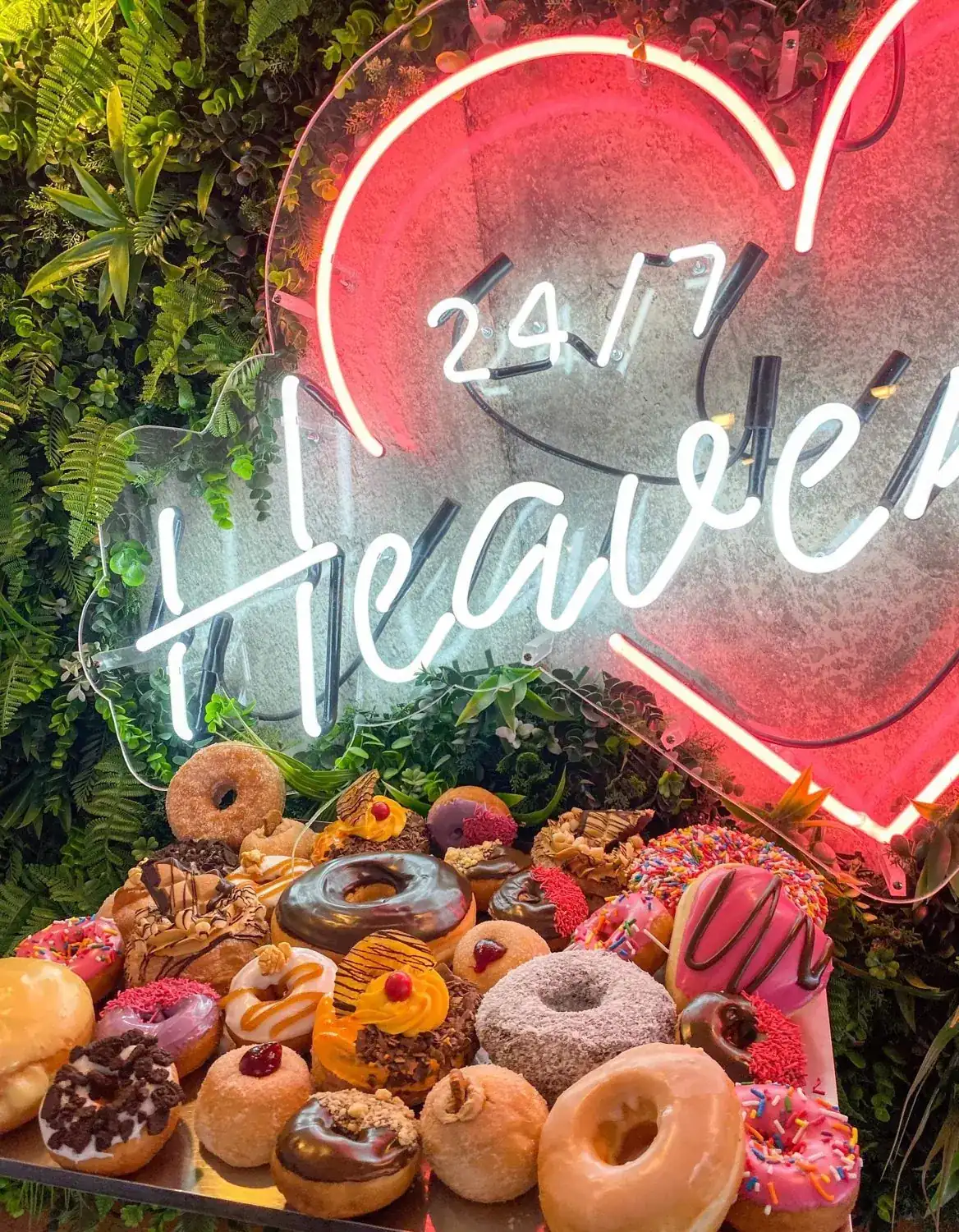 The 24/7 Heaven neon heart above a tray of iced donuts.