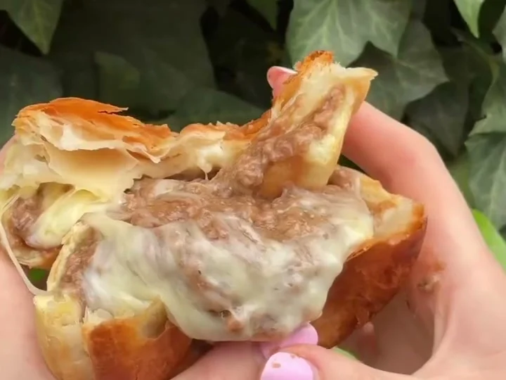 A beef and triple cheese pie torn open, showing the beef filling and melted cheese.